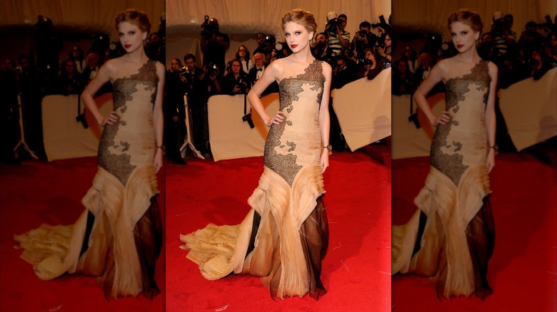 Taylro Swift wearing a pink gown with black lace accents on the red carpet