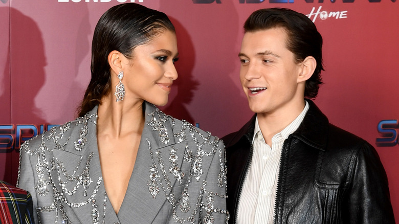 Zendaya smiling over at Tom Holland as they pose at a 