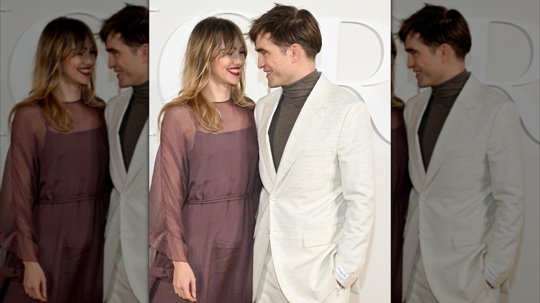 Suki Waterhouse and Robert Pattinson smiling at each other as they stand close for photos