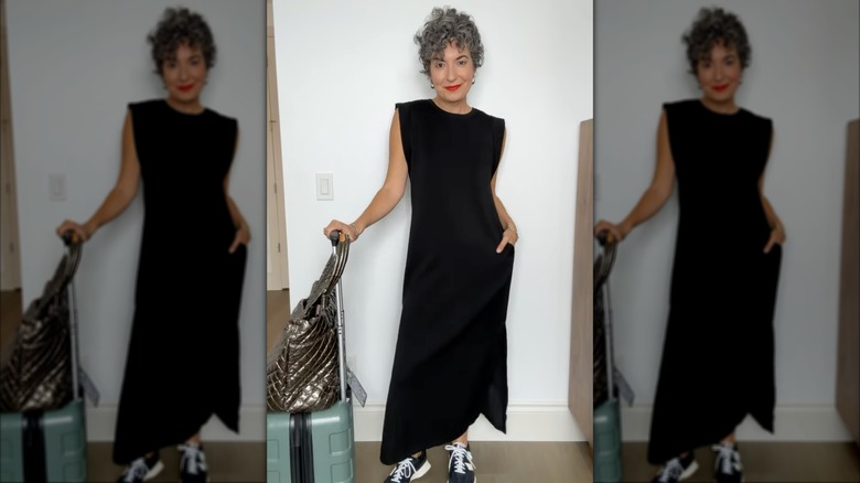 A woman in a long black dress and sneakers with her suitcase