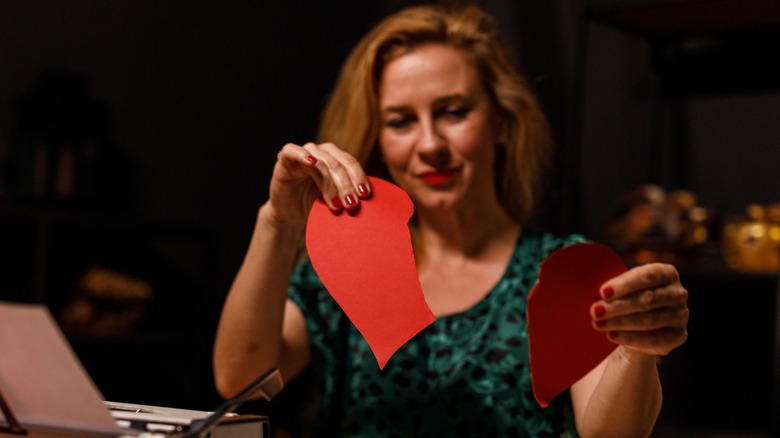 A woman ripping up a red paper heart