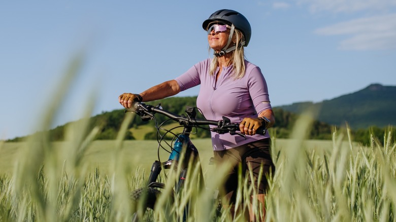 A smiling woman cycling alone in a field wearing sunglasses and a helmet