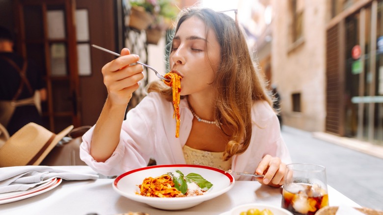 A woman with her eyes closed eating pasta from a bowl