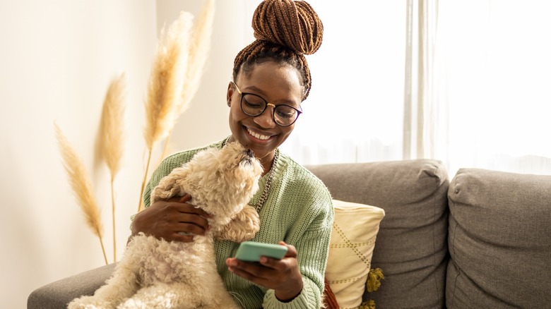 A woman petting a dog while smiling at her phone