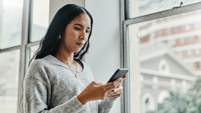 A woman in a gray top with a neutral expression texting