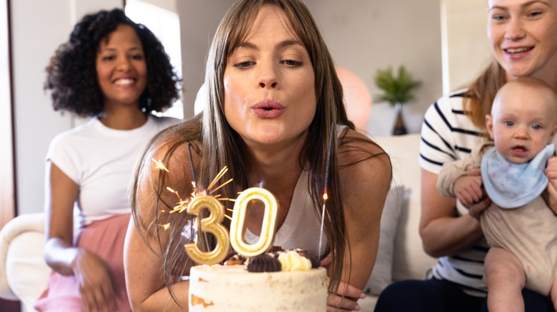 A woman blowing out 30th birthday candles on a cake