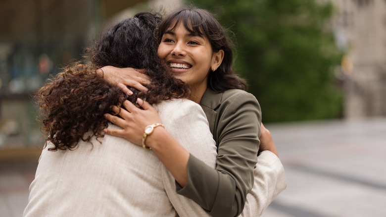 Two women hugging, one is smiling and the other has her back to the camera