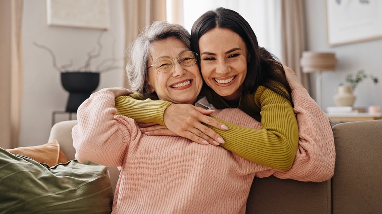 An older and younger woman hugging while the older woman sits on a sofa