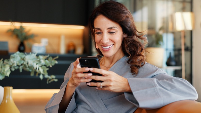 A woman smiling at her phone while sitting down