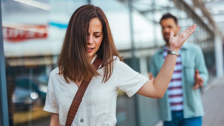 An annoyed woman with her hand up while walking away from a man