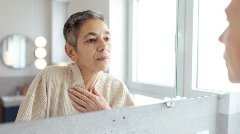 A woman looking at herself in the mirror with her hand over her heart