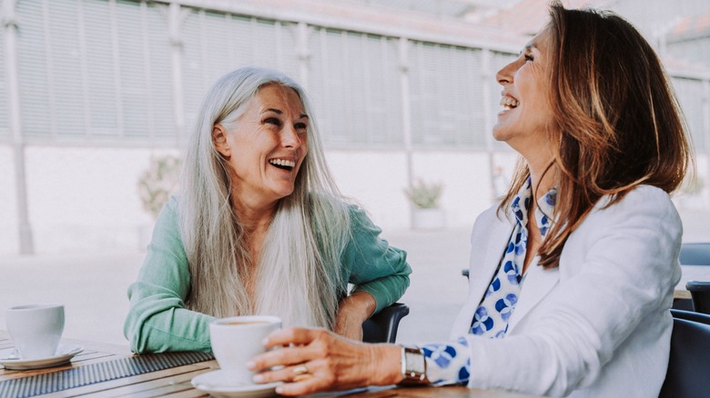 Two older women laughing while sitting at a table