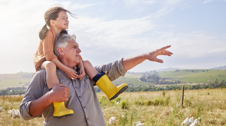 A granddaughter sitting on her grandpa's shoulders while outdoors