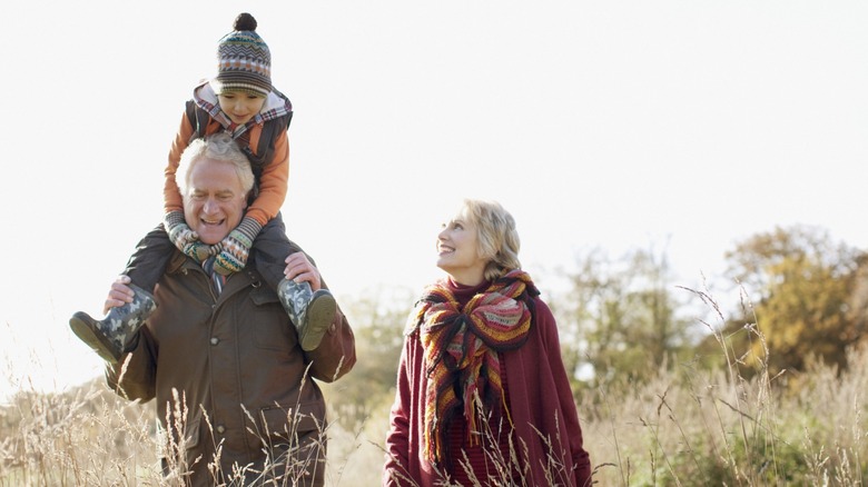 A grandfather with his grandchild on his shoulders while walking with his wife