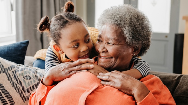 A grandmother embracing her young granddaughter while sitting on the sofa