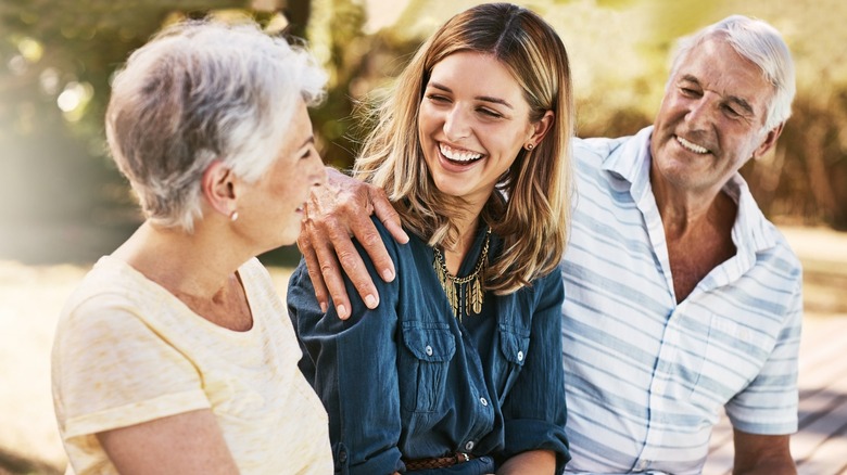 A younger woman smiling while sitting in between her two grandparents