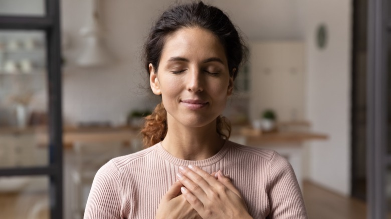 A woman with her eyes closed and slightly smiling with her hands over her heart
