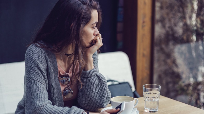 A woman sitting at a table and looking worried with her hand to her mouth