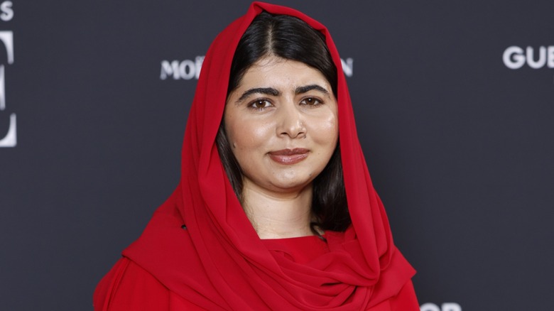 Malala Yousafzai slightly smiling on the red carpet in a red outfit