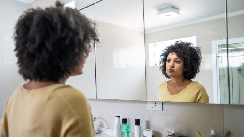 A woman looking at herself in the mirror with a forlorn expression