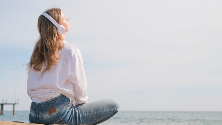 A woman listening to music while sitting by the ocean