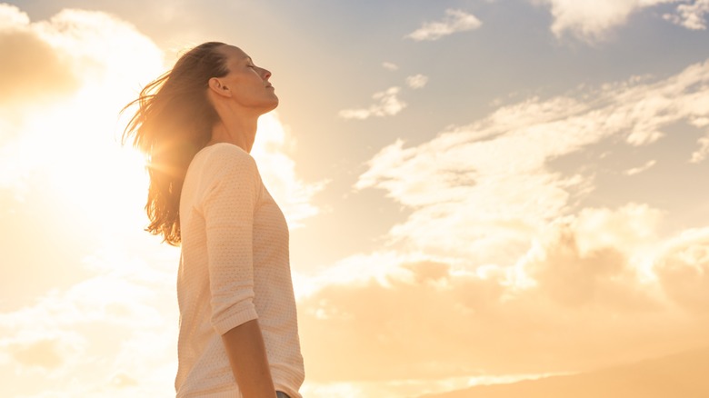 A woman with her eyes closed standing below a lit sky with clouds