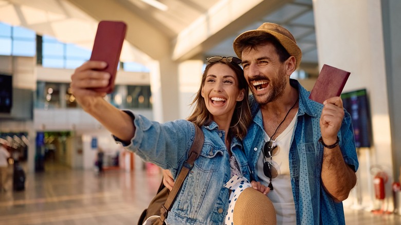 A couple smiling and taking a selfie at the airport