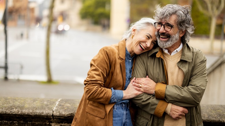 An older couple embracing while standing outside, with the woman resting her head on the man's shoulder