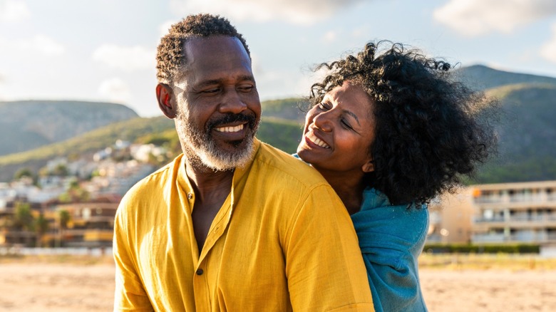 A couple embracing at the beach, with the woman hugging the man from behind