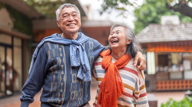 An older couple walking outside while the man puts his arm around the woman