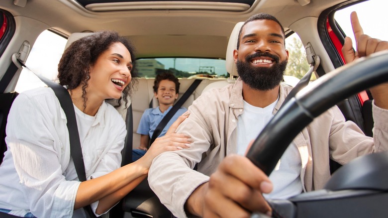 A woman singing to a man in the car with a child in the backseat, all are smiling