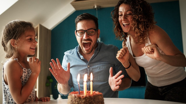 A man celebrating his birthday with a cake alongside his wife and daughter