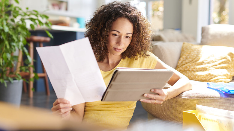 Woman holding paper looking at tablet