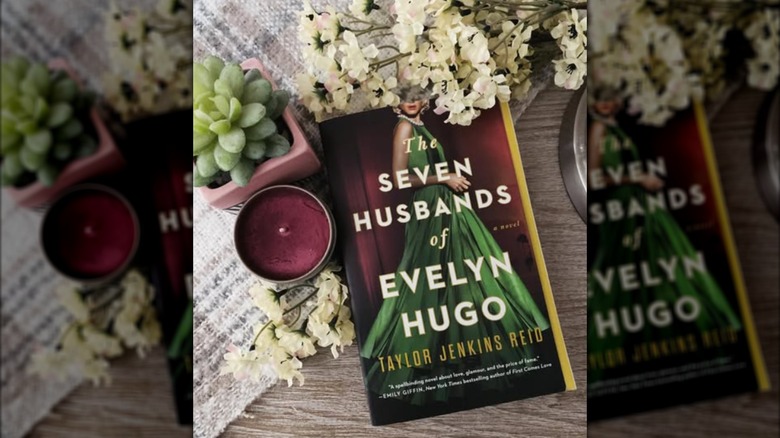 A copy of the book "The Seven Husbands of Evelyn Hugo" laying on a table next to a candle and fresh flowers