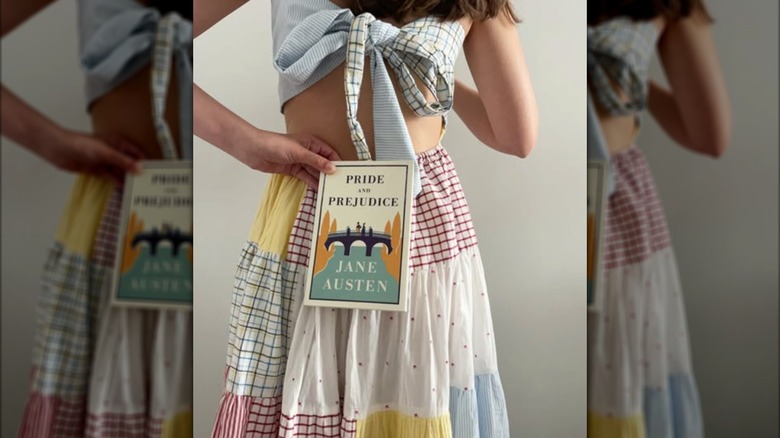 A woman holding a copy of the novel "Pride & Prejudice" behind her back