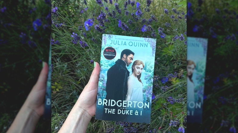 A hand holding a copy of "The Duke & I" in front of a bush of lavender