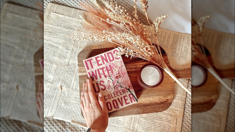 A copy of the novel "It Ends With Us" on a cutting board next to a candle and dried flowers