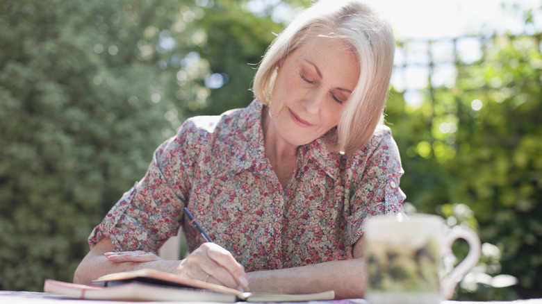 Older woman sits outside and writes in her journal