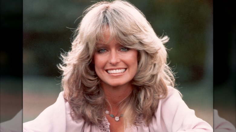 Farrah Fawcett smiling with voluminous hair and understated makeup during a 1975 photoshoot