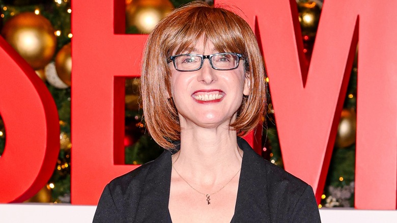 Freida McFadden smiling on the red carpet while wearing a red, bob wig