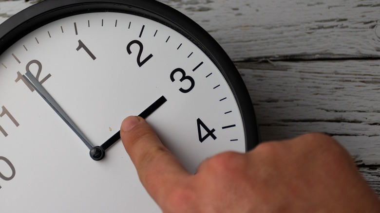 A finger touching the hands on an analog clock