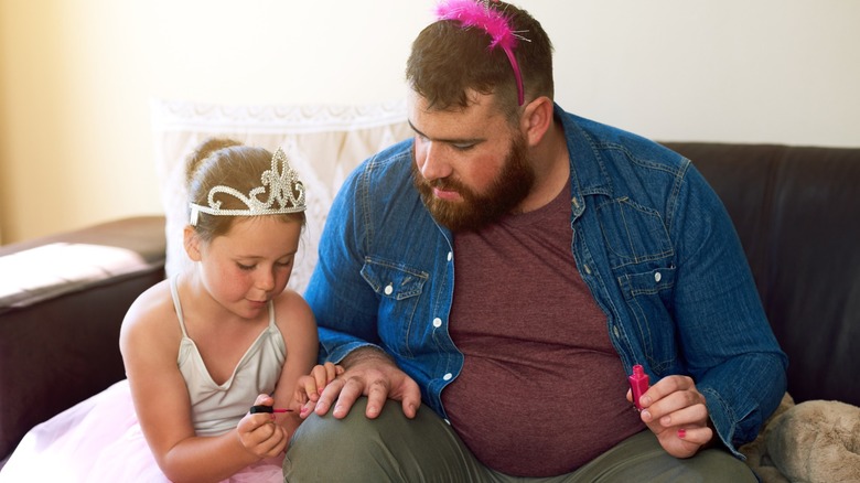 A little girl painting her dad's nails
