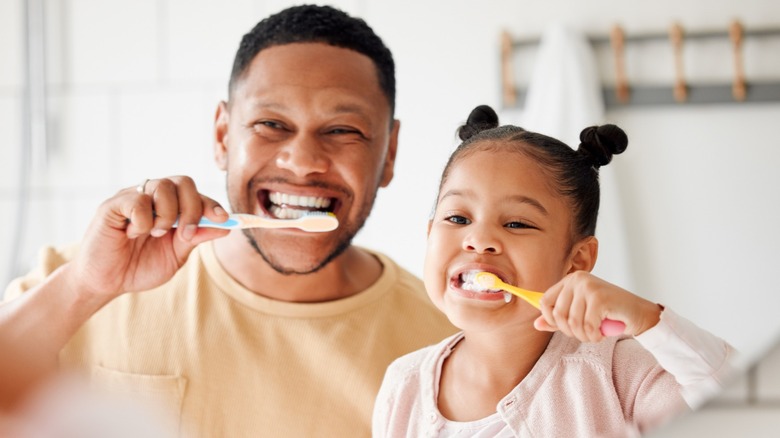 A dad and daughter brushing their teeth in the mirror