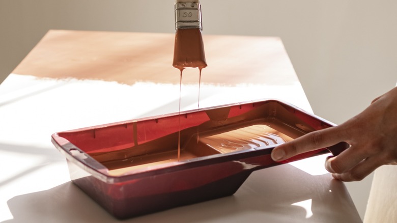 A paintbrush dripping over a tray containing orange paint