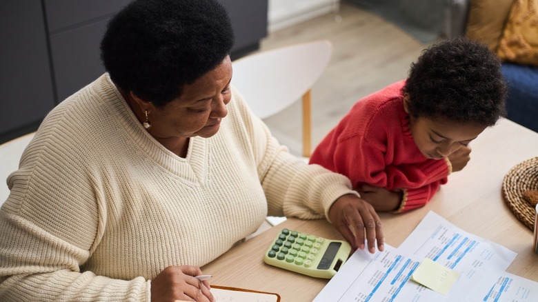An adult woman and young boy using a calculator to work out bills