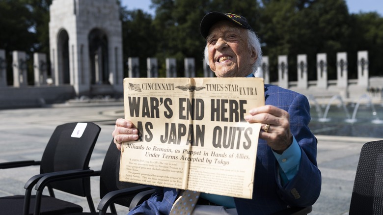 A war veteran holding up a newspaper declaring the end of World War II