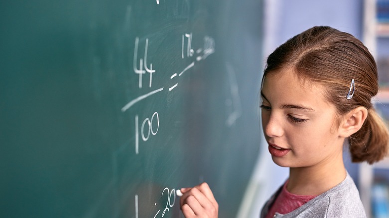 A young girl writing fractions on a chalkboard