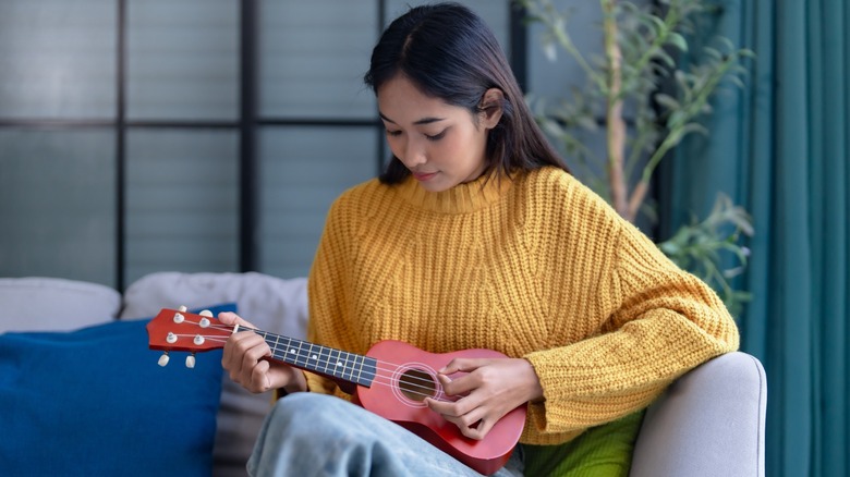 A woman in a yellow sweater playing the ukelele