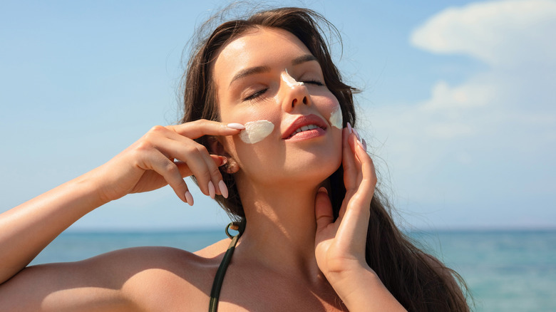 Woman on the beach putting sunscreen on face