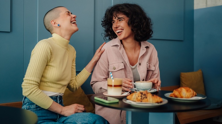 Two friends laughing while sitting at a table